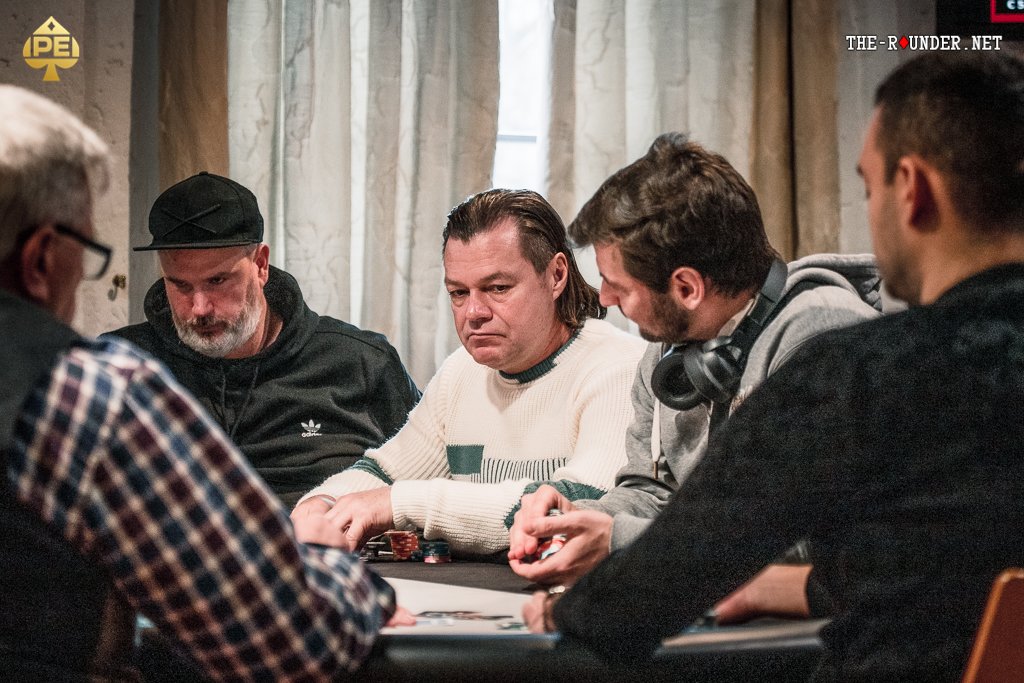 Ein Bild von vier Personen, die an einem Pokertisch sitzen und Karten spielen. Es herrscht eine entspannte Atmosphäre, während sie ihre Karten prüfen. Die Spieler sind konzentriert und vertie