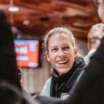 Ein Mann und eine Frau sitzen an einem Pokertisch und spielen eine Partie Poker. Der Mann hält Karten in der Hand, während die Frau konzentriert auf ihre eigenen Karten schaut. Im Hintergrund sind Poker