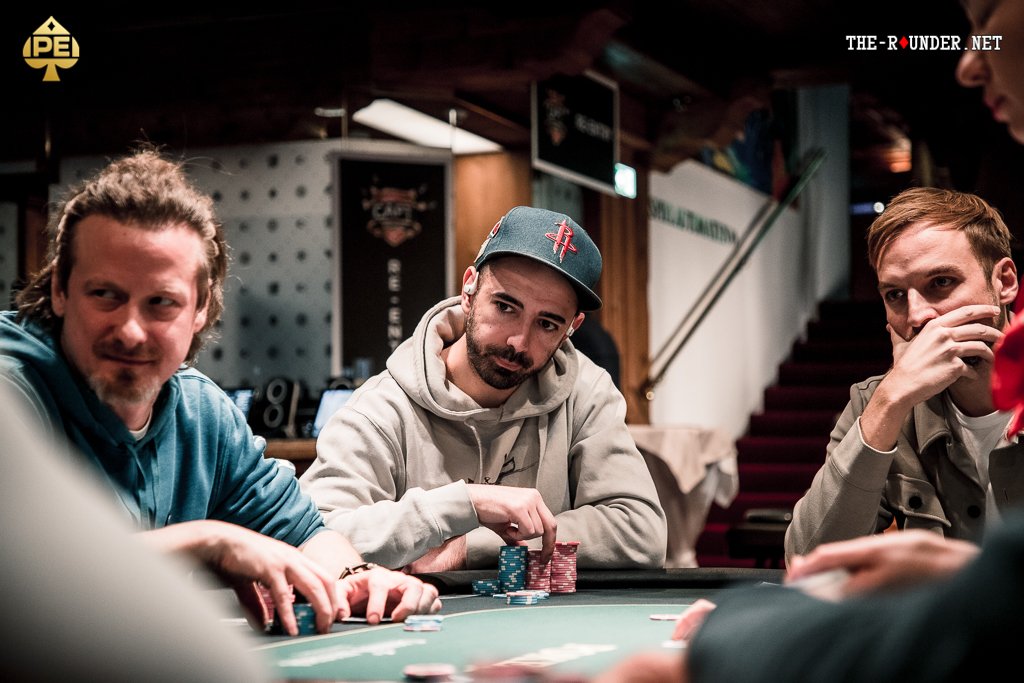 Ein Mann und eine Frau sitzen an einem Pokertisch in einem eleganten Raum. Der Mann hat gerade seine Karten aufgedeckt und schaut selbstbewusst, während die Frau gespannt auf ihre Karten schaut.