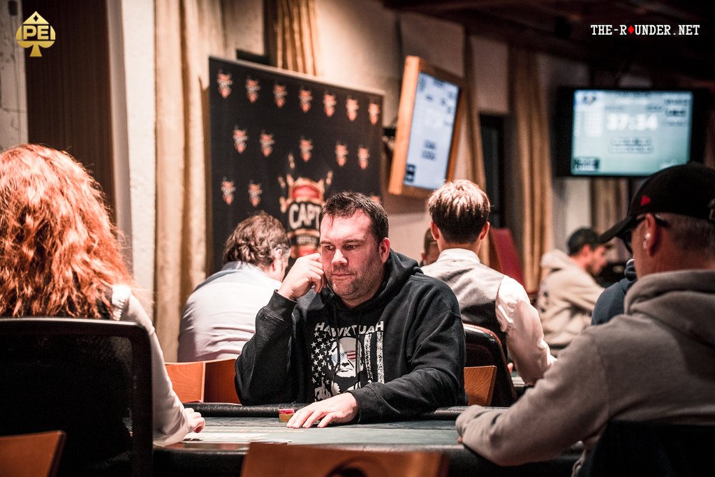 Ein Mann und eine Frau sitzen an einem Pokertisch und spielen Poker. Der Mann hält Karten in der Hand, während die Frau konzentriert auf ihre Karten schaut. Im Hintergrund sind Pokerchips und Get