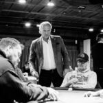 Ein Mann und eine Frau spielen Poker in einem eleganten Casino. Der Mann hat Karten in der Hand, während die Frau konzentriert auf ihre Chips schaut. Die Atmosphäre ist luxuriös mit einem Kronleuchter im