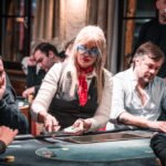 Ein Poker-Tisch mit Spielkarten, Pokerchips und Getränken, umgeben von vier Personen, die konzentriert spielen.