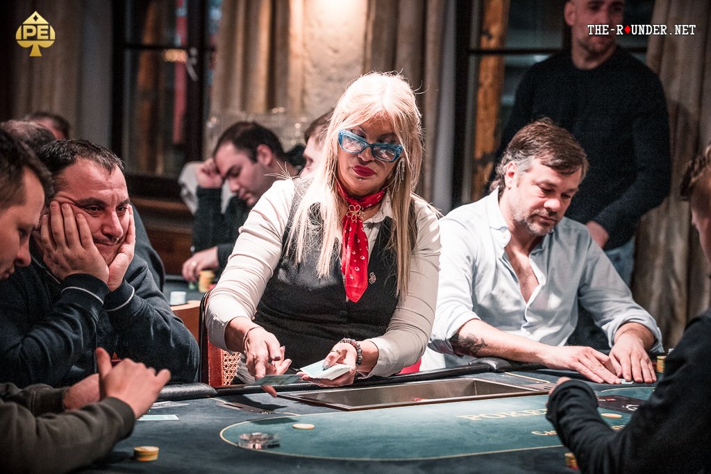 Ein Poker-Tisch mit Spielkarten, Pokerchips und Getränken, umgeben von vier Personen, die konzentriert spielen.