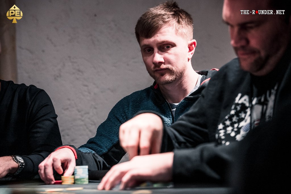 Ein Mann und eine Frau sitzen an einem Pokertisch und betrachten konzentriert ihre Karten. Die Frau hat einen Stapel Chips vor sich, während der Mann seine Hand auf seinen Karten hält. Das Bild strahlt