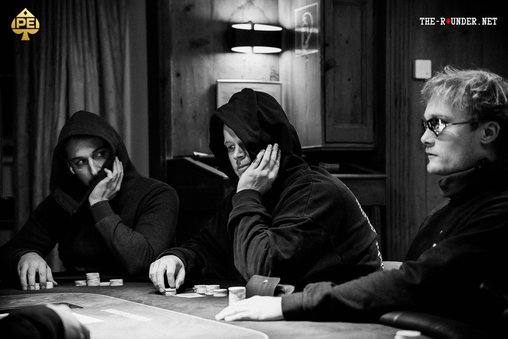 Ein professioneller Pokertisch mit grünem Filz, umgeben von Stühlen und Pokerchips. Spieler sitzen um den Tisch herum und halten ihre Karten.