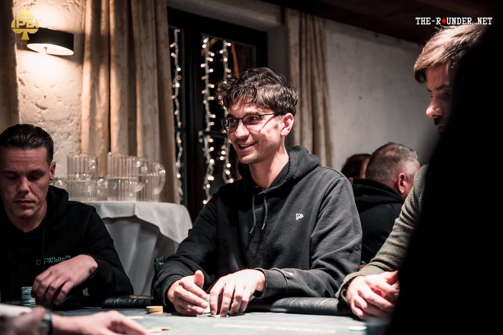 Ein Spieler wirft Pokerchips in die Mitte des Tisches während einer Pokerrunde in einem Casino. In der Mitte des Tisches sind Karten und weitere Chips zu sehen.