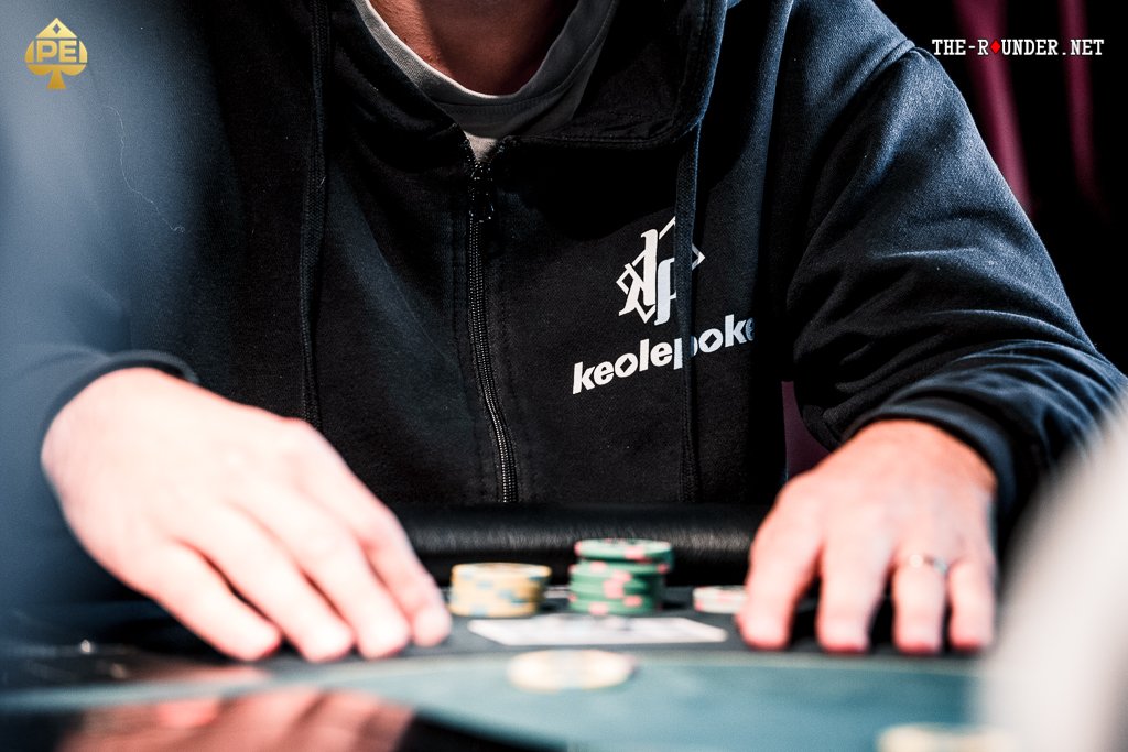 Ein Mann und eine Frau sitzen an einem Pokertisch und konzentrieren sich auf ihre Karten. Der Mann hat eine Kappe auf und die Frau trägt eine Brille. In der Mitte des Tisches liegen Pokerch