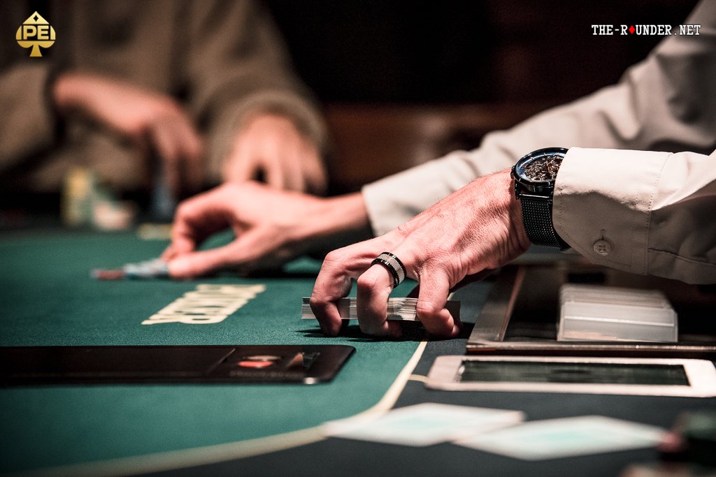Ein Mann und eine Frau sitzen an einem Pokertisch und spielen Karten. Der Mann hält seine Karten in der Hand, während die Frau mit einem konzentrierten Blick auf ihre Karten schaut. Die Szene wirkt