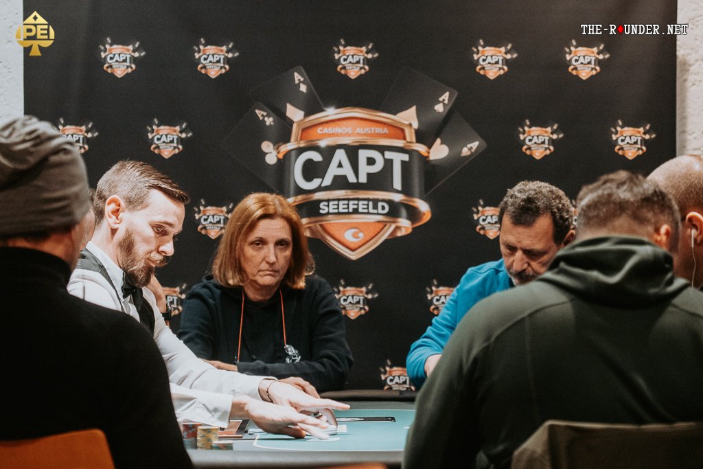 Ein Mann spielt Poker an einem Tisch mit grünen Filz. Er hält Karten in der Hand und starrt konzentriert auf seine Chips. Im Hintergrund sind andere Spieler und eine Glühbirne zu