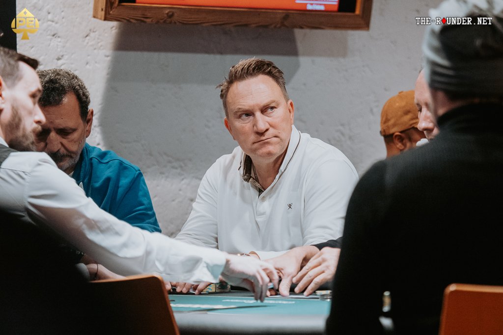 Ein Mann und eine Frau sitzen an einem Pokertisch und spielen Texas Hold'em. Sie halten Karten in der Hand und schauen konzentriert auf die Gemeinschaftskarten in der Mitte des Tisches. Eine gemüt