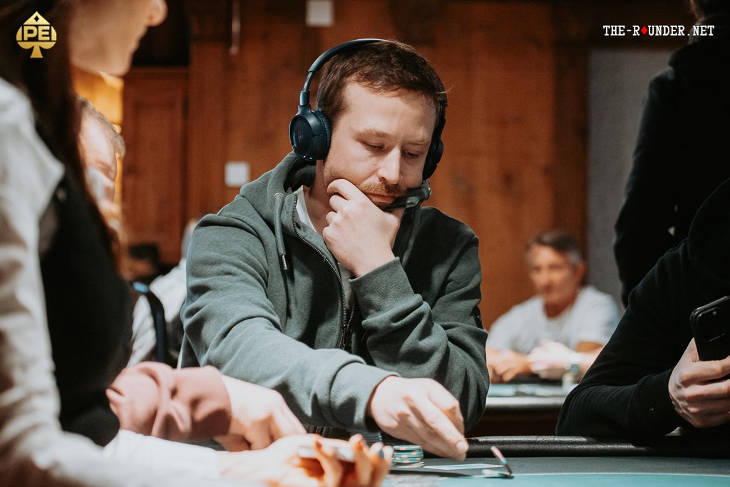 Ein professioneller Pokertisch mit grüner Filzdecke, umgeben von Stühlen und Chips, während Spieler Karten halten und ihre Einsätze platzieren.