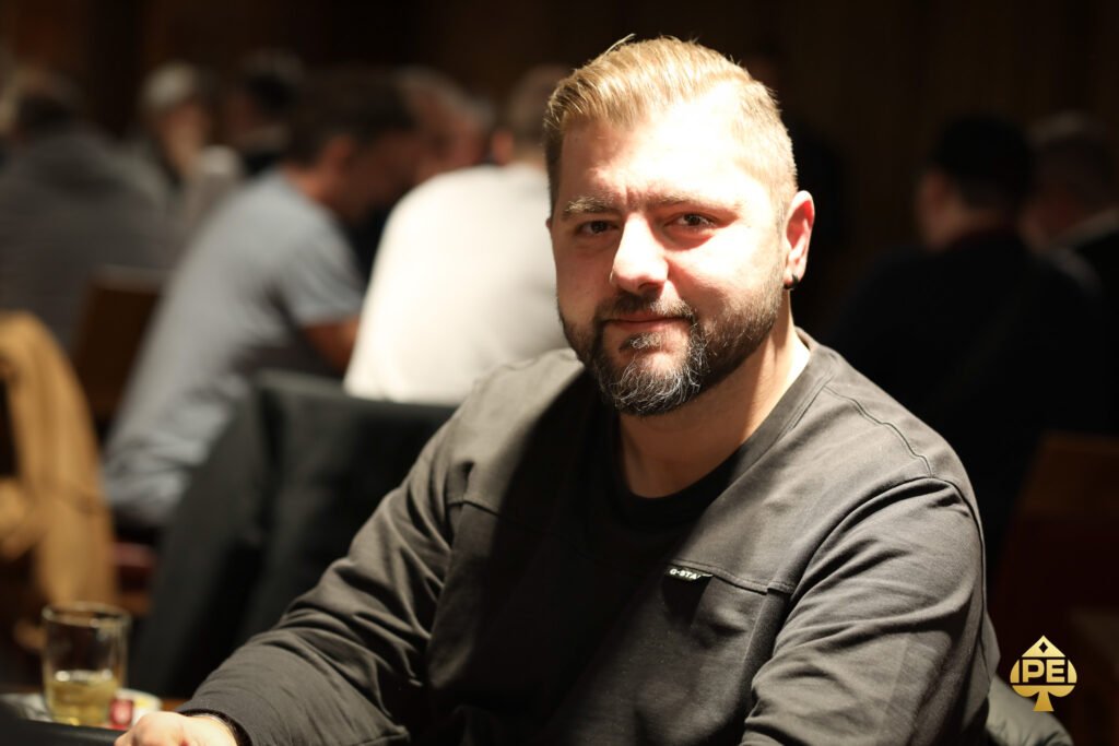 Ein Mann und eine Frau sitzen lächelnd an einem Pokertisch und halten jeweils Karten in der Hand. Im Hintergrund sind Pokerchips und Getränke zu sehen.