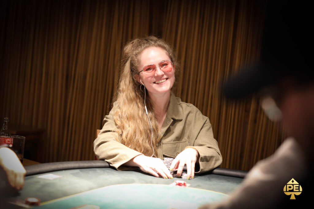 Ein professioneller Pokertisch mit grünem Filz und eleganten Holzverzierungen, umgeben von Stühlen mit roten Polstern. Spieler sitzen um den Tisch herum und halten ihre Karten während eines