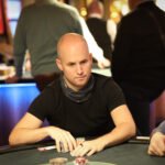 Ein Mann und eine Frau spielen eine Partie Poker in einem eleganten Casino. Der Mann hat Karten in der Hand, während die Frau konzentriert auf ihre Karten schaut. Die Szene ist durch die luxuriöse Ein