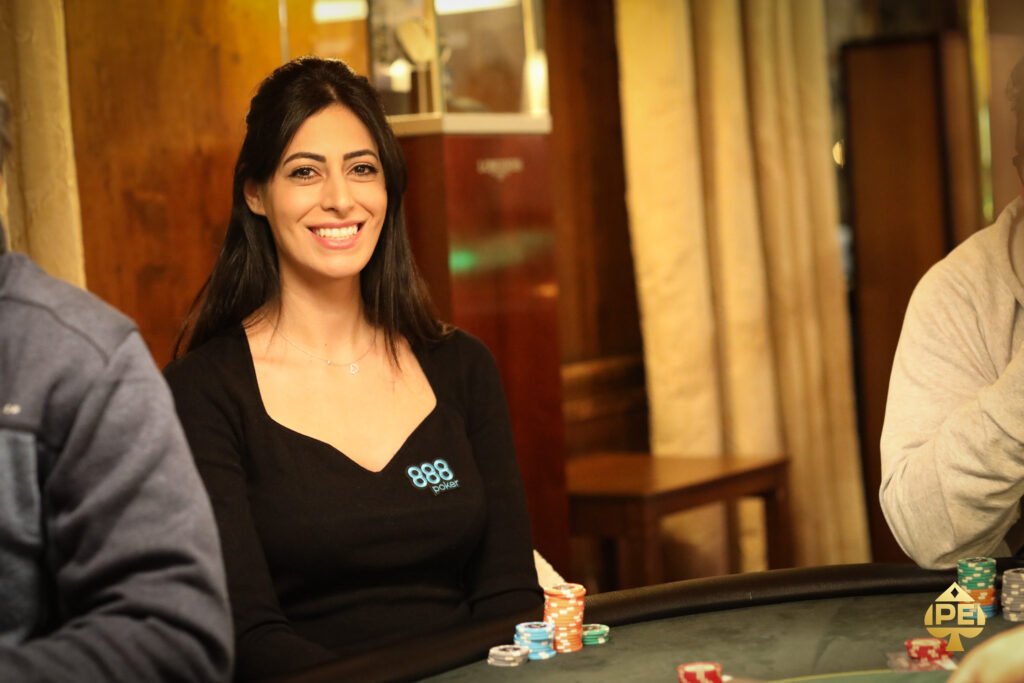 Ein Mann in einem dunkelblauen Anzug und einer roten Krawatte sitzt an einem Pokertisch und hält eine Hand mit Spielkarten. In seinem Gesichtsausdruck ist Konzentration und Ernsthaftigkeit