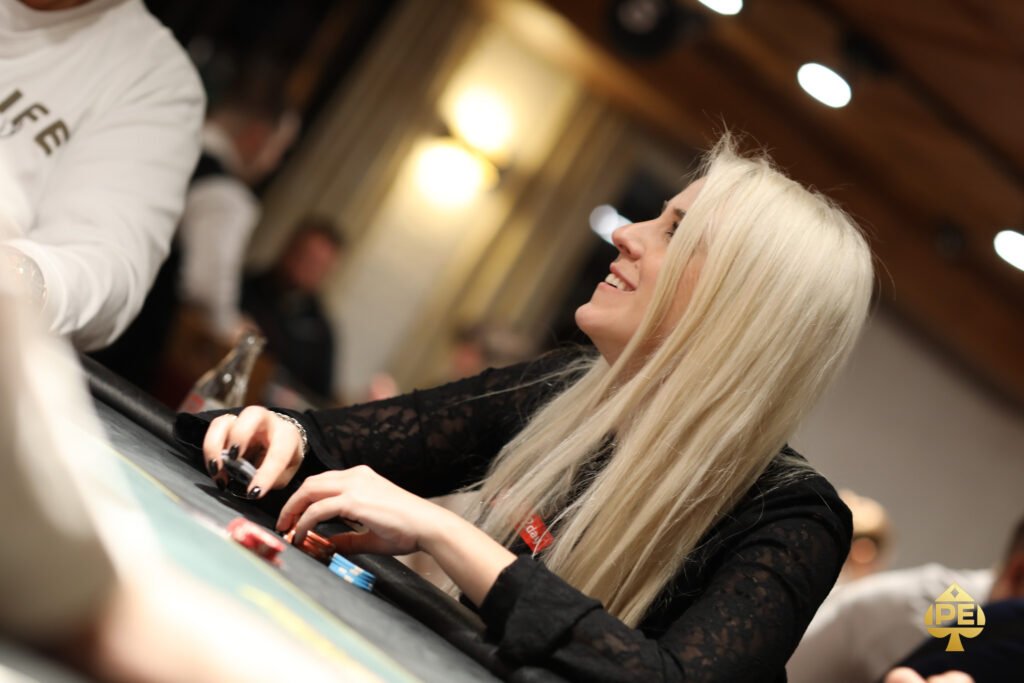 Ein Mann und eine Frau sitzen an einem Pokertisch, sie haben Karten in der Hand und schauen konzentriert auf den Tisch. Im Hintergrund sind Pokerchips und Getränke zu sehen.