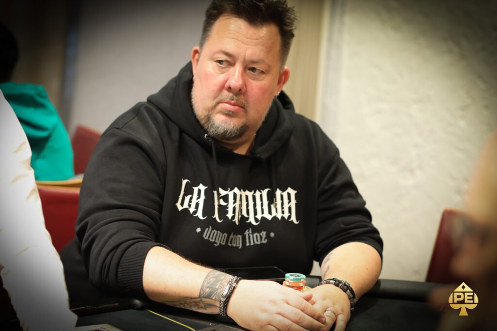 Ein Mann spielt Poker an einem Tisch in einem eleganten Casino mit grünen Filzdecken und goldenen Getränkehaltern. Er hat einen ernsten Gesichtsausdruck und hält Karten in der