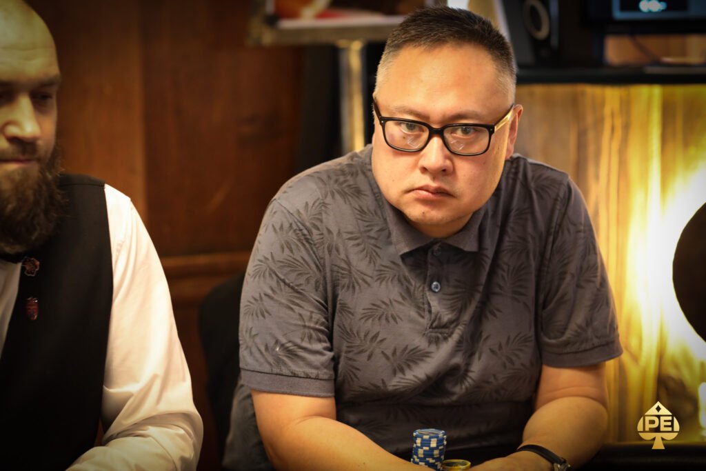 Ein professioneller Pokerspieler sitzt an einem Tisch voller Pokerchips und Karten während er konzentriert auf seine Hand schaut.