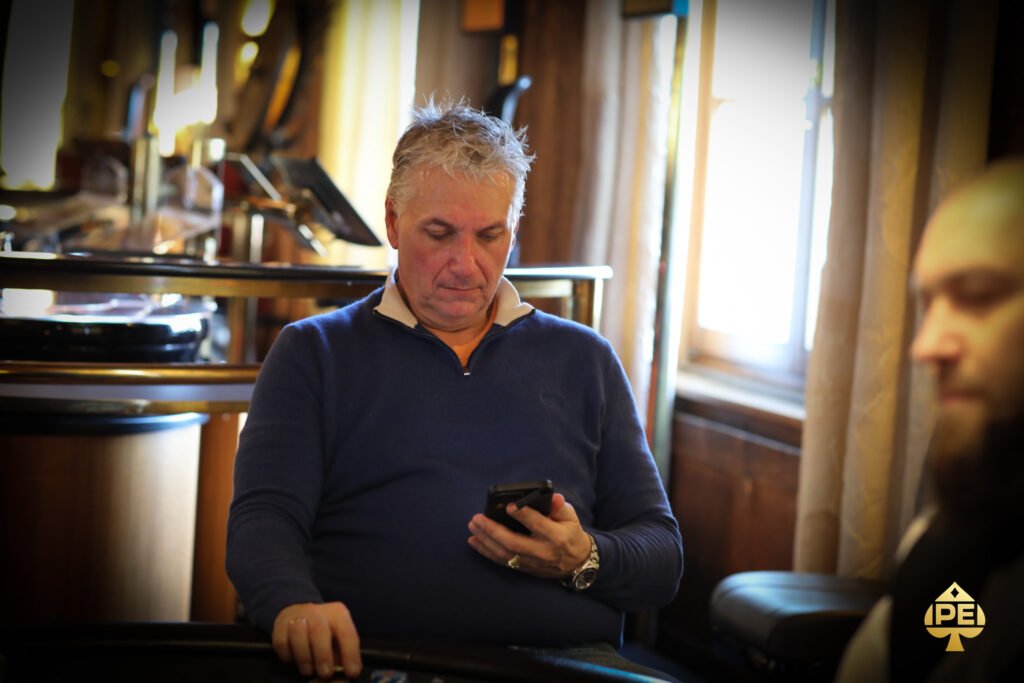 Ein professioneller Pokerspieler mit Sonnenbrille und Kappe sitzt an einem grünen Pokertisch und hält seine Karten in der Hand, während er konzentriert auf seine Gegner schaut.