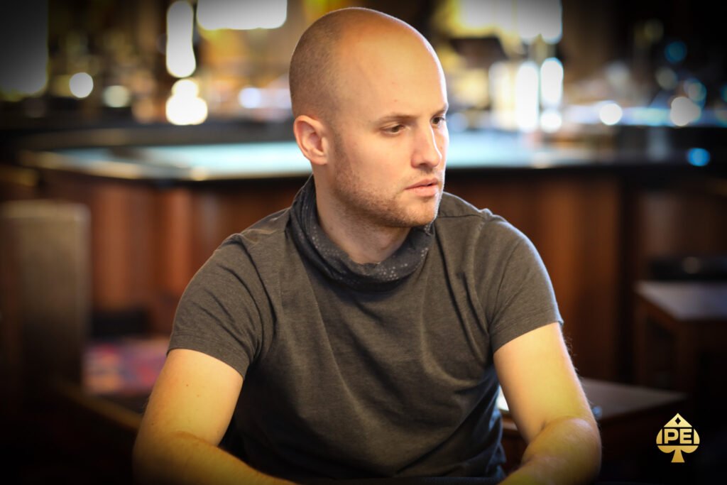 Ein Mann und eine Frau sitzen zusammen an einem Pokertisch und spielen Karten. Sie haben konzentrierte Gesichtsausdrücke und halten ihre Karten in der Hand. Im Hintergrund sind Pokerchips und Get