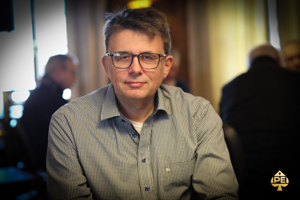 Ein Mann und eine Frau sitzen an einem Pokertisch und spielen Poker. Der Mann hat eine Hand voll Spielchips und schaut konzentriert auf seine Karten, während die Frau lächelnd ihre Karten betrachtet