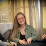 Ein Mann und eine Frau sitzen an einem Pokertisch und spielen Texas Hold'em. Der Mann hat eine Hand mit Karten, während die Frau nachdenklich ihre Chips betrachtet. Im Hintergrund sind weitere Spieler und ein Dealer