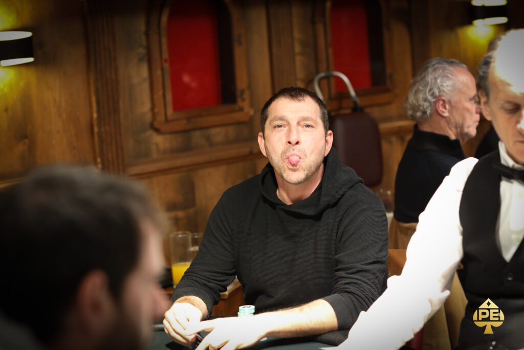 Ein professioneller Pokerspieler mit Sonnenbrille und Kappe, der konzentriert an einem Pokertisch sitzt und Karten hält, während er seine Gegner beobachtet.