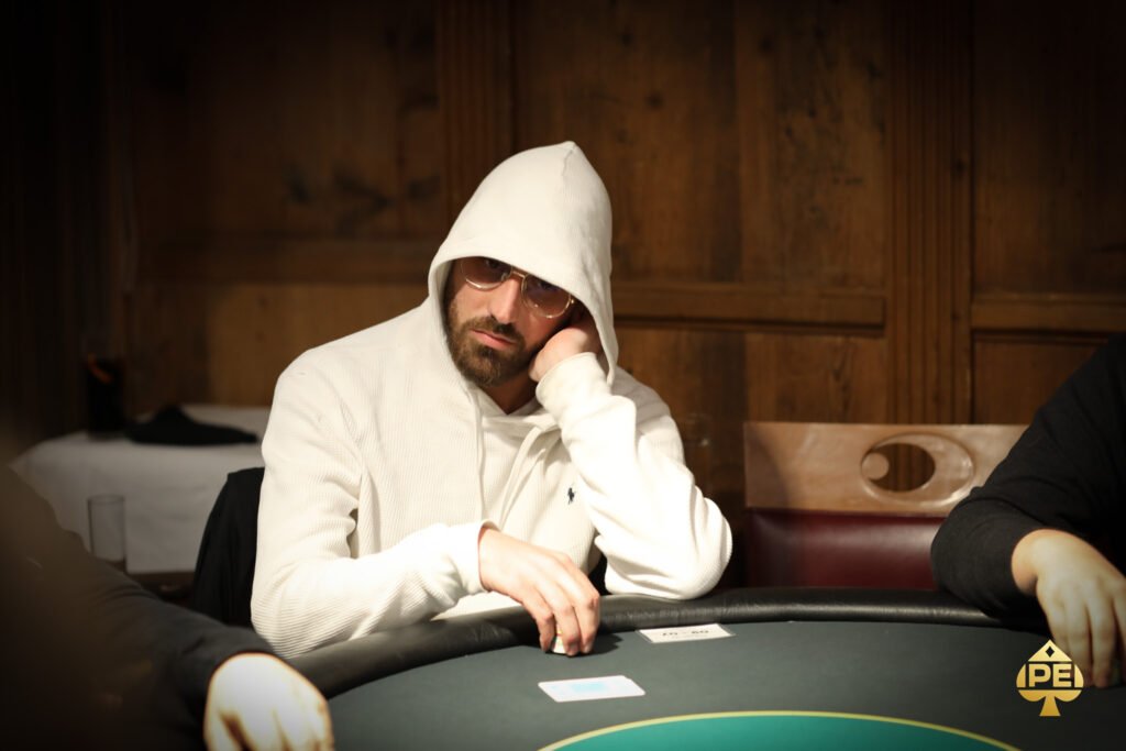 Ein professioneller Pokerspieler konzentriert sich am Pokertisch, umgeben von Chips und Karten, während er seine Hand betrachtet.