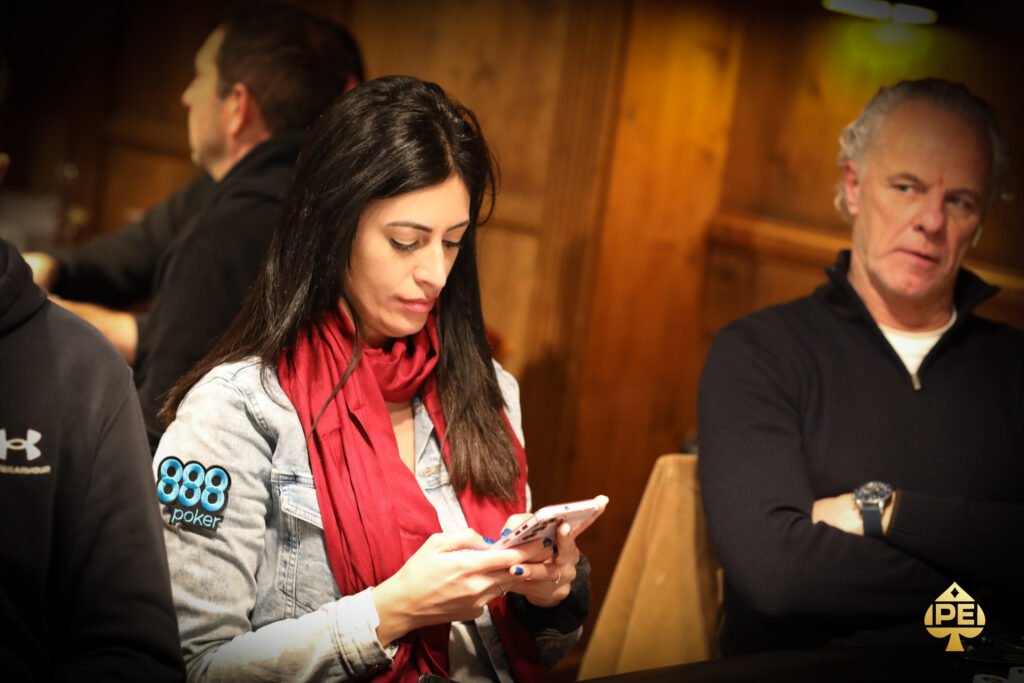 Ein Gruppenfoto von vier Personen, die gemeinsam an einem Pokertisch sitzen und Karten spielen. Zwei Männer und zwei Frauen sind konzentriert und lächeln während des Spiels. Es gibt Pokerchips und Spiel