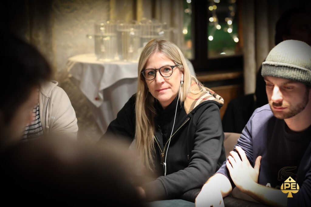 Ein Mann und eine Frau sitzen an einem Pokertisch und spielen Poker. Der Mann hat Karten in der Hand und schaut konzentriert auf den Tisch, während die Frau ihm gegenüber mit einem Pokerchip spielt und lä