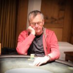 Ein Mann und eine Frau sitzen an einem Pokertisch in einem eleganten Casino. Der Mann hält Karten in der Hand und schaut konzentriert auf den Tisch, während die Frau mit einem selbstbewussten Blick in