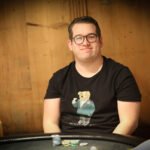 Ein Mann und eine Frau spielen Poker an einem eleganten Tisch in einem stilvollen Raum mit Kronleuchter und Gemälden.