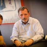 Ein Mann und eine Frau sitzen an einem Pokertisch und spielen Karten. Der Mann hat eine Hand mit Pokerchips und schaut konzentriert auf seine Karten, während die Frau lächelnd ihre Karten betracht