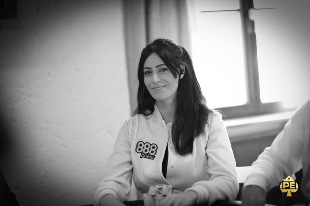 Ein Tisch mit grünem Filz, auf dem Spielkarten, Pokerchips und Getränke platziert sind, umgeben von vier Personen, die Poker spielen.
