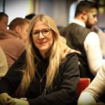 Ein professioneller Pokertisch mit grünem Filz, umgeben von Stühlen und Pokerchips. In der Mitte des Tisches liegen Karten mit verschiedenen Werten und Farben. Im Hintergrund sind unschar