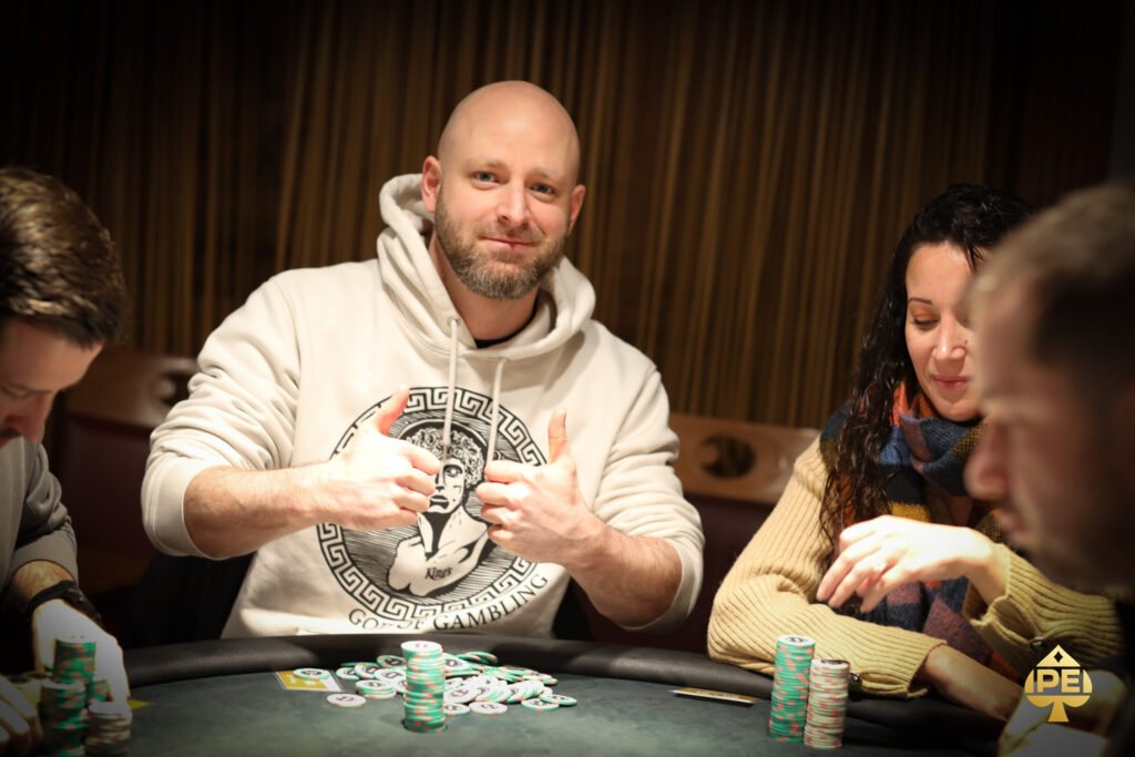 Ein Mann sitzt an einem Pokertisch und betrachtet seine Karten mit ernstem Gesichtsausdruck, umgeben von anderen Spielern. Die Atmosphäre ist konzentriert und spannungsgeladen.