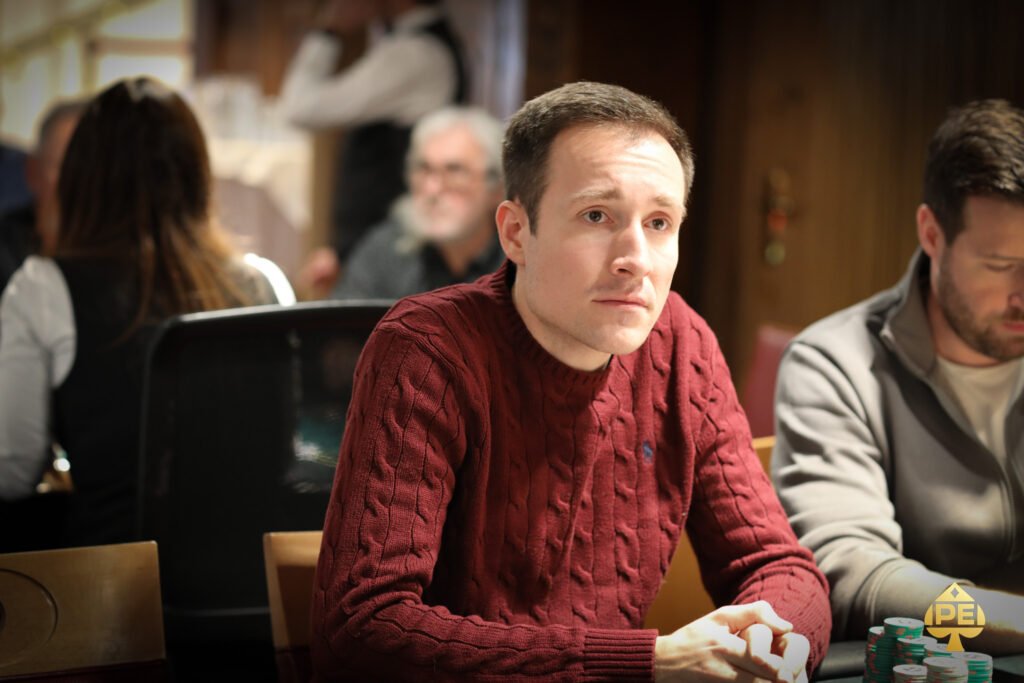 Ein Mann und eine Frau sitzen an einem Pokertisch und betrachten ihre Karten. Der Mann hat eine Zigarre im Mund und die Frau trägt eine elegante Abendgarderobe. Im Hintergrund sind Pokerchips