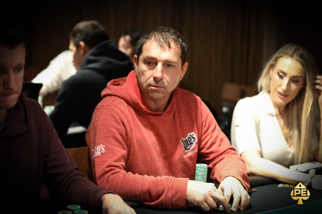 Ein Mann und eine Frau spielen Poker an einem eleganten Tisch in einem luxuriösen Casino. Der Mann hat Karten in der Hand, während die Frau mit ernstem Gesichtsausdruck auf ihre Karten schaut. Das
