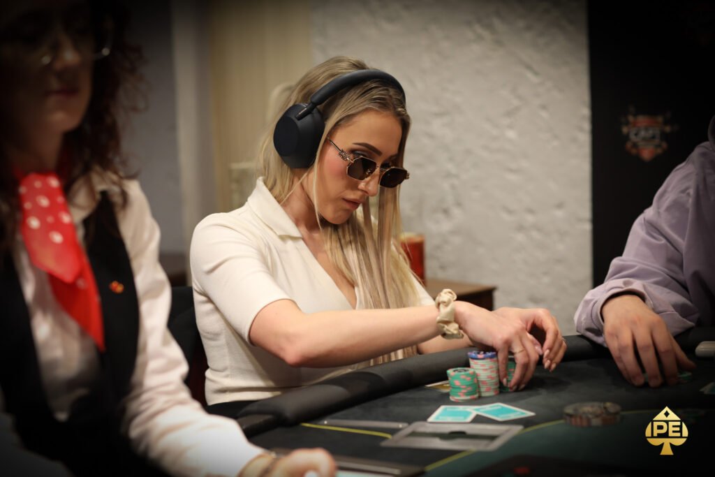 Ein Mann spielt Poker an einem Tisch in einem eleganten Casino. Er hat einen ernsten Gesichtsausdruck und hält Karten in der Hand, während Chips vor ihm auf dem Tisch liegen. Im Hintergrund