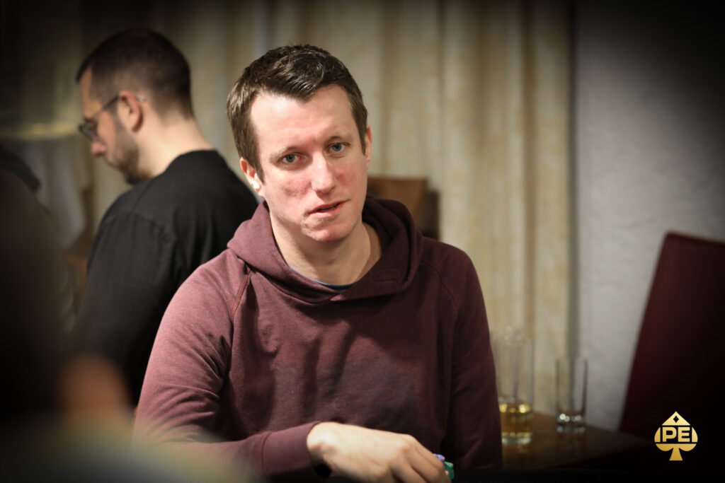 Ein Mann und eine Frau sitzen an einem Pokertisch und betrachten konzentriert ihre Karten. Im Hintergrund sind Pokerchips und Spielkarten zu sehen.