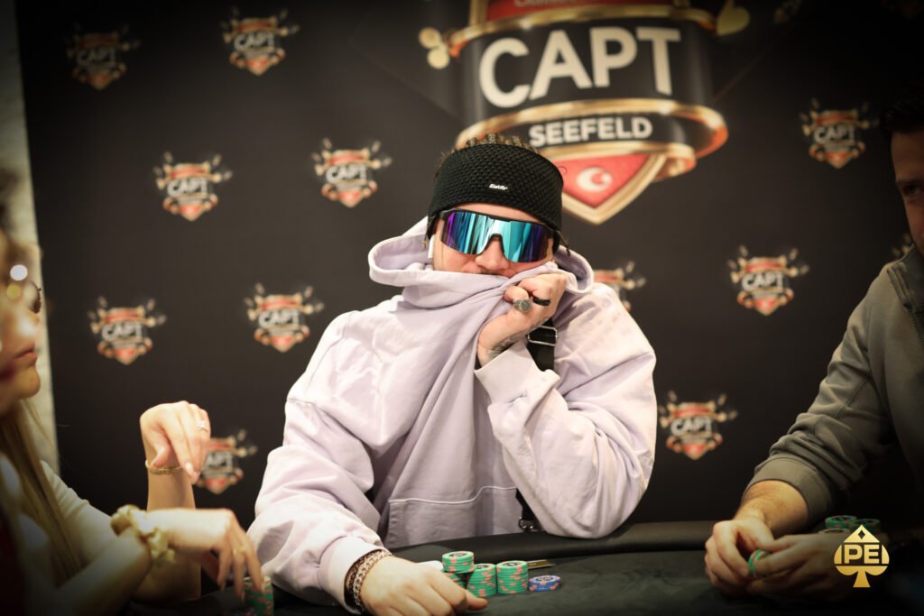 Ein Mann und eine Frau sitzen an einem Pokertisch und spielen Karten. Der Mann hat eine Hand voll Karten, während die Frau nachdenklich auf ihre Karten schaut. Im Hintergrund sind Pokerchips und Get