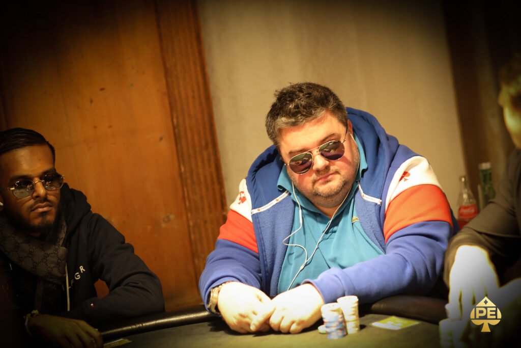 Ein professioneller Pokerspieler mit Sonnenbrille und Kappe konzentriert sich auf sein Blatt während eines Turniers.