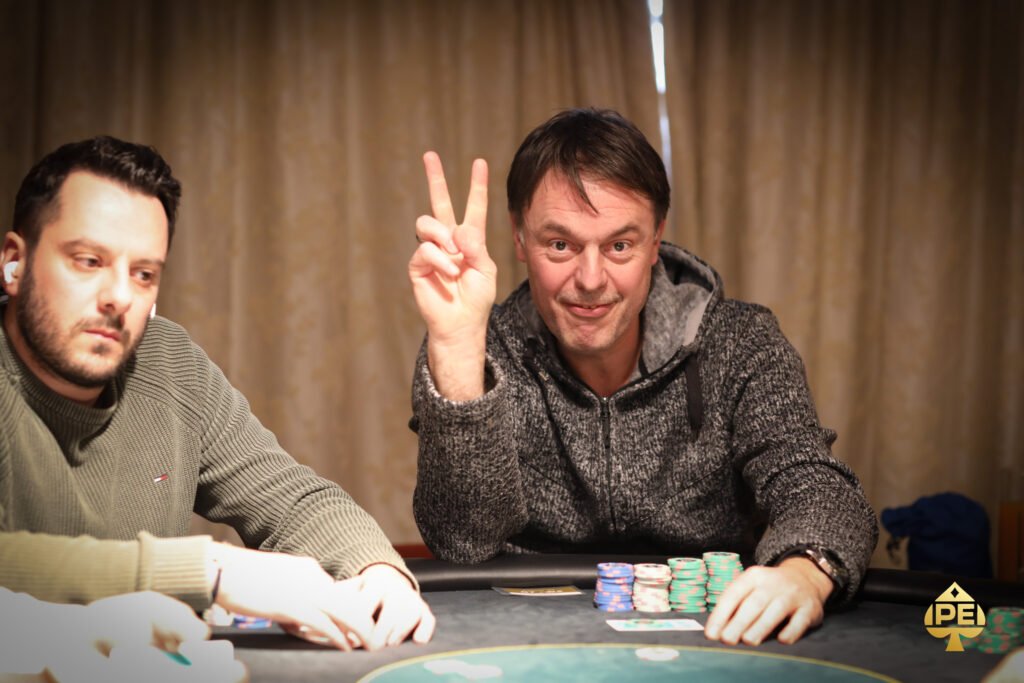 Ein Mann und eine Frau sitzen an einem Pokertisch und spielen Texas Hold'em. Der Mann hat eine große Hand mit Pokerchips vor sich, während die Frau nachdenklich ihre Karten betrachtet. Die Szene spielt