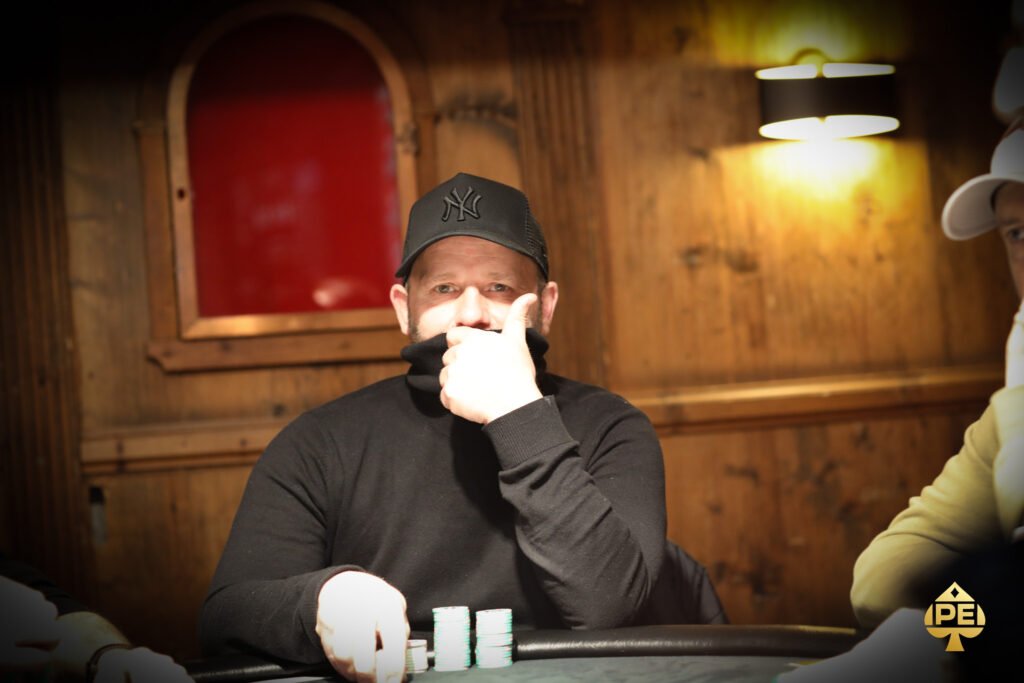 Ein Mann spielt Poker an einem eleganten Tisch in einem stilvollen Casino, umgeben von anderen Spielern und einer glamourösen Atmosphäre.
