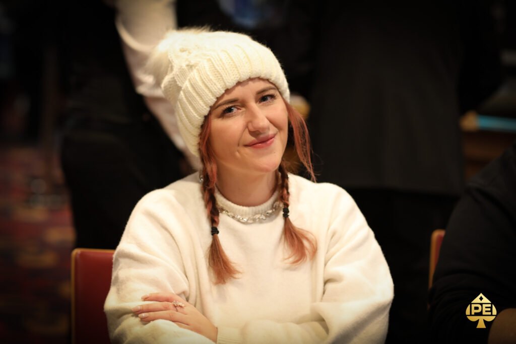 Ein Mann und eine Frau sitzen an einem Pokertisch und spielen gegeneinander. Der Mann hat eine Hand mit Pokerchips und schaut konzentriert auf seine Karten, während die Frau eine Hand an ihre Stirn h