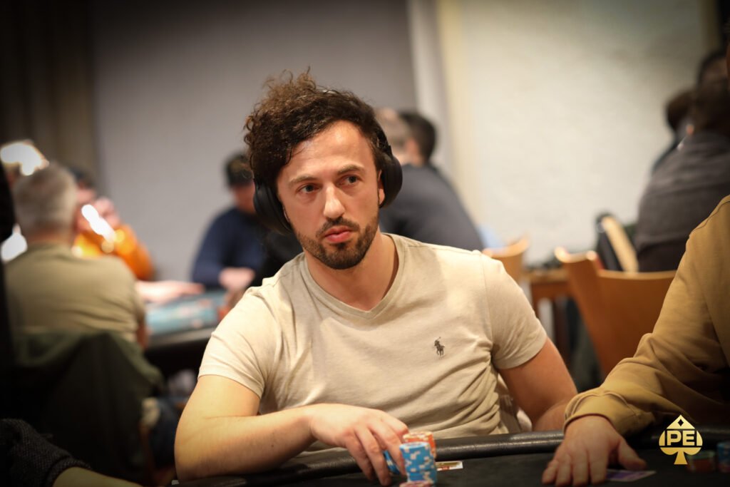 Ein Mann und eine Frau sitzen an einem Pokertisch und spielen eine Partie Poker. Der Mann hält Karten in der Hand, während die Frau konzentriert auf ihre eigenen Karten schaut. Im Hintergrund sind Poker