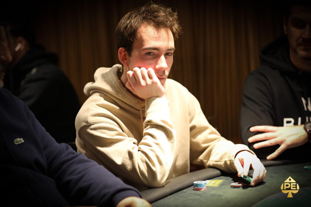Ein Mann sitzt an einem Pokertisch, umgeben von Chips und Karten, während er konzentriert auf seine Hand schaut.