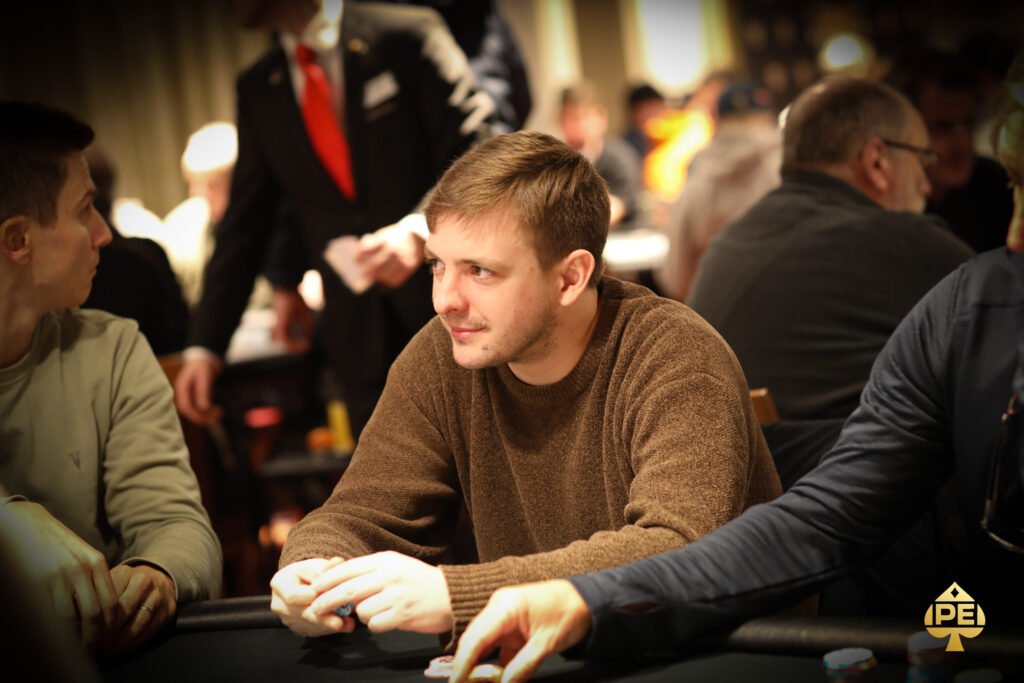 Ein Mann sitzt an einem Pokertisch mit Chips und Karten vor sich. Er hat eine ernsthafte Miene und scheint konzentriert zu sein.