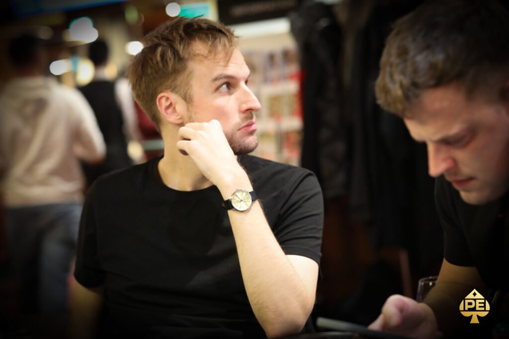 Ein Mann und eine Frau spielen Poker an einem eleganten Tisch in einem luxuriösen Casino. Der Mann hat Karten in der Hand und konzentriert sich auf das Spiel, während die Frau mit einem selbstbewussten Blick auf