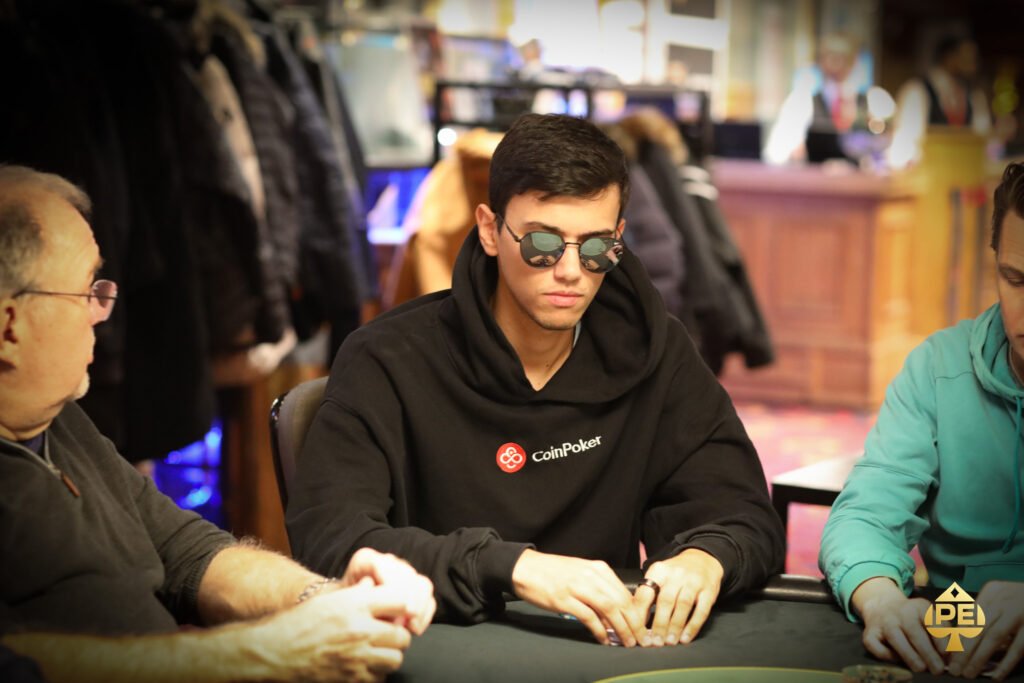 Ein Mann und eine Frau sitzen an einem Pokertisch und betrachten ihre Karten. Die Frau hat eine Hand am Kinn und schaut konzentriert auf ihre Karten, während der Mann neben ihr seine Karten betrachtet
